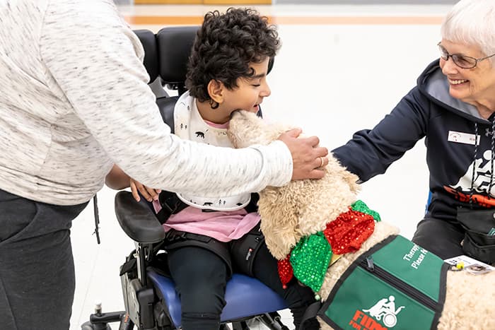 A goldendoodle kisses a Cedar Lane student in a wheelchair.