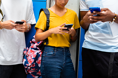 Close-up of teen high school students using mobile phone in school corridor.