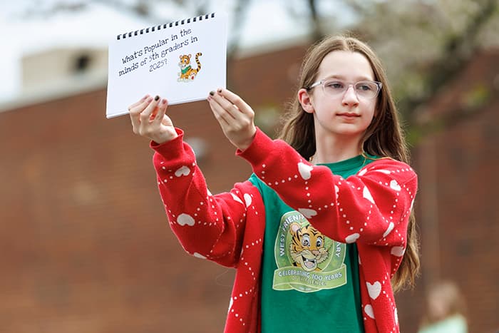 A 5th grade student holds up “What’s Popular in the Minds of 5th Graders in 2025?,” which was an item added to the time capsule to be opened in 2050.