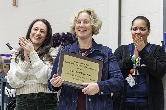 Nicki Meshbesher holding an award while two female colleagues clap.