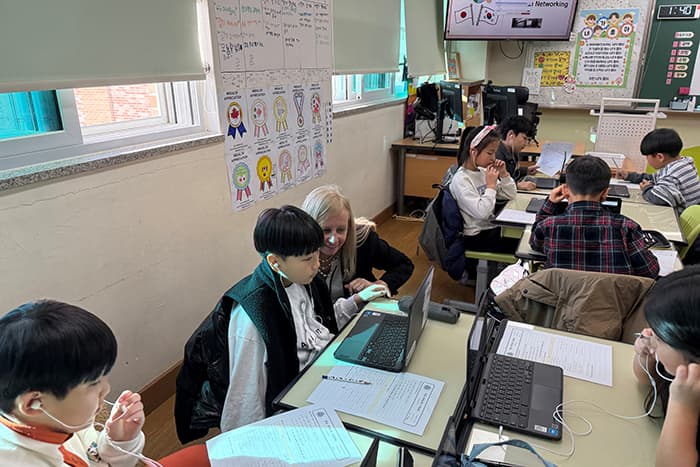 Jen Robinson in a classroom observing a South Korean student working on a computer.