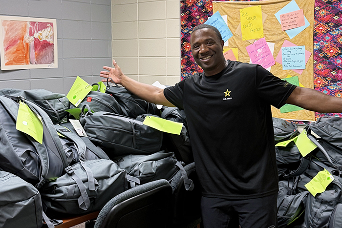 A volunteer in front of a pile of packed backpacks.