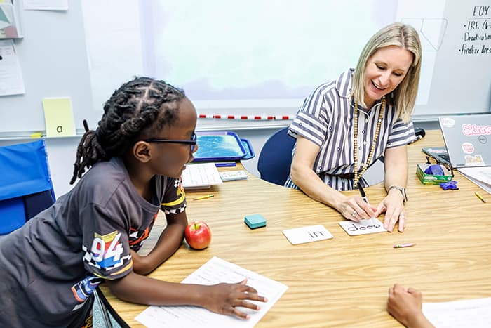 A Special Ed teacher sitting and teaching a student.